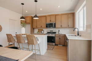 Kitchen with stainless steel appliances, decorative light fixtures, light stone countertops, light wood-style floors, and a kitchen breakfast bar