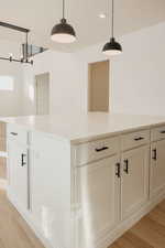 Kitchen with a large island, white cabinets, light wood-type flooring, and light stone counters