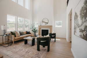 Living area with a tile fireplace, light wood finished floors, and a high ceiling