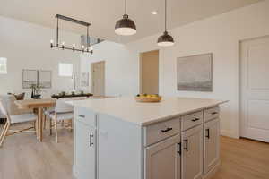 Kitchen featuring decorative light fixtures, a center island, light wood-style flooring, white cabinets, and light stone counters