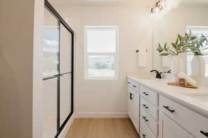 Bathroom featuring double vanity, light wood finished floors, and an enclosed shower
