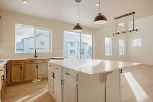 Two tone kitchen with light wood-style flooring, a center island, decorative light fixtures, two tone cabinetry, and backsplash