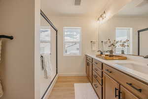 Bathroom featuring double vanity, light wood-type flooring, and a shower stall