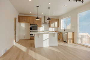 Kitchen featuring backsplash, light wood finished floors, stainless steel appliances, hanging light fixtures, and a kitchen breakfast bar