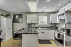 Kitchen featuring a kitchen bar, stainless steel appliances, white cabinets, updated paint and lights, and light wood-style floors