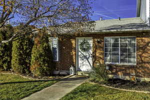 View of exterior entry featuring brick siding and a yard