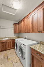 Laundry area with stone tile floors, cabinet space, washer and clothes dryer, and a textured ceiling