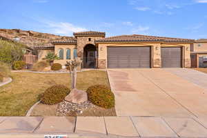 Mediterranean / spanish-style home featuring stone siding, stucco siding, a tiled roof, and concrete driveway