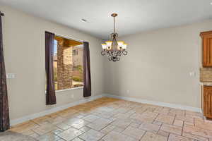 Unfurnished dining area featuring stone tile flooring and suspended lighting