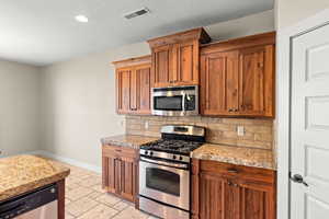 Kitchen featuring stainless steel appliances, tasteful backsplash, wood finish cabinetry, stone tile floors, and recessed lighting