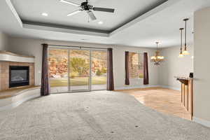 Unfurnished living room with hanging lights, ceiling fan, a tile fireplace, stone tile flooring, and a raised ceiling
