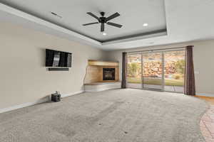 Unfurnished living room with a tile fireplace, recessed lighting, a raised ceiling, a ceiling fan, and light colored carpet