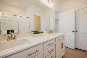 Bathroom featuring double vanity, light wood finished floors, and a stall shower