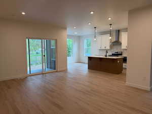 Kitchen featuring open floor plan, light countertops, a kitchen island with sink, backsplash, and hanging light fixtures