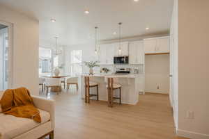 Kitchen with a kitchen bar, white cabinets, a center island with sink, light wood finished floors, and stainless steel appliances