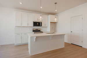 Kitchen with white cabinetry, pendant lighting, stainless steel appliances, and light wood-type flooring