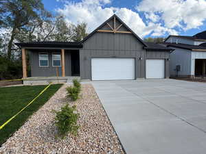 View of front of property with board and batten siding, a garage, covered porch, and concrete driveway