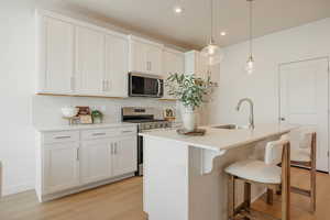 Kitchen featuring stainless steel appliances, an island with sink, light wood-style flooring, a breakfast bar, and decorative backsplash
