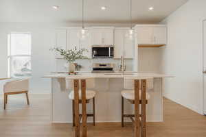 Kitchen featuring white cabinets, light wood-type flooring, hanging light fixtures, a center island with sink, and tasteful backsplash