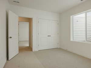 Unfurnished bedroom with light carpet and a closet
