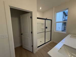 Bathroom with a shower stall, double vanity, light wood-style floors, and recessed lighting