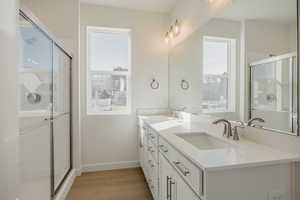 Full bathroom featuring a stall shower, double vanity, light wood-style flooring, and plenty of natural light