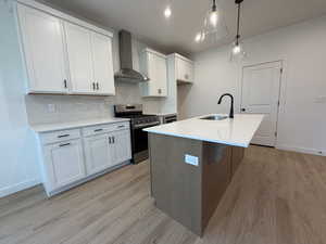 Two tone kitchen featuring stainless steel range with gas cooktop, an island with sink, light stone counters, backsplash, and light wood finished floors