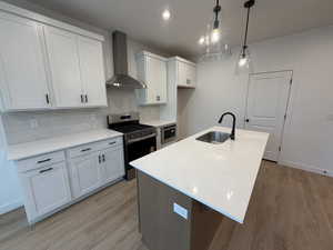 Kitchen with an island with sink, stainless steel appliances, tasteful backsplash, white cabinetry, and light wood-style floors