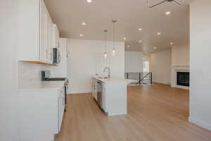 Kitchen featuring white cabinets, stainless steel appliances, pendant lighting, light wood-type flooring, and open floor plan