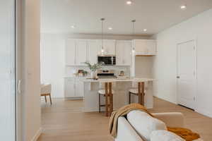 Kitchen with a kitchen island with sink, light wood-type flooring, pendant lighting, a kitchen breakfast bar, and white cabinetry