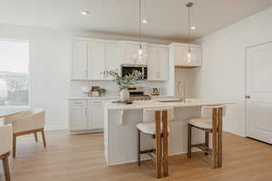 Kitchen featuring light wood-style flooring, white cabinetry, an island with sink, and a kitchen bar