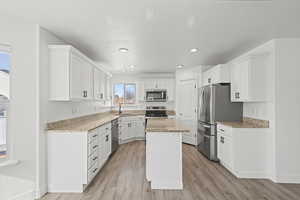 Kitchen featuring white cabinets, stainless steel appliances, light stone counters, light wood finished floors, and recessed lighting