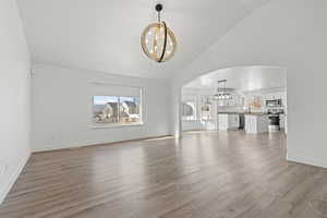 Unfurnished living room with arched walkways, hanging lights, light wood-style flooring, and vaulted ceiling