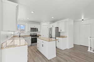 Kitchen featuring a kitchen island, stainless steel appliances, white cabinets, light wood-style floors, and recessed lighting