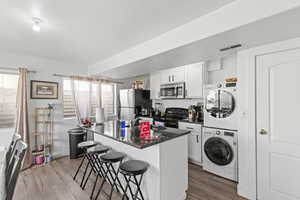Kitchen featuring a kitchen bar, white cabinetry, stainless steel appliances, a kitchen island with sink, and dark wood finished floors