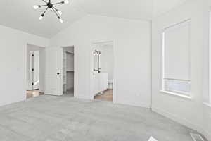 Unfurnished bedroom featuring a chandelier, a spacious closet, light colored carpet, and ensuite bath