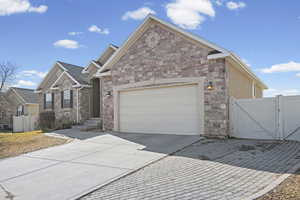 View of front of house with driveway, a gate, stone siding, and a garage