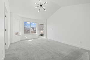Carpeted spare room with hanging lights and vaulted ceiling