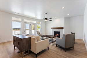 Living area featuring light wood-style flooring, a lit fireplace, ceiling fan, recessed lighting, and a textured ceiling