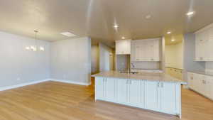 Kitchen with light stone countertops, white cabinets, and light wood-type flooring