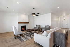 Living room with light wood-style floors, a lit fireplace, recessed lighting, and a ceiling fan