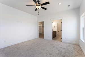 Unfurnished bedroom with light colored carpet, a walk in closet, ceiling fan, recessed lighting, and ensuite bath