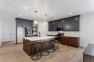 Kitchen with a breakfast bar area, stainless steel appliances, open shelves, an island with sink, and light wood finished floors