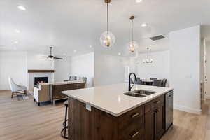 Kitchen with open floor plan, dark wood finish cabinetry, a breakfast bar, a lit fireplace, and a center island with sink
