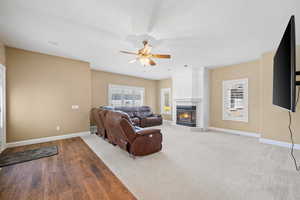 Carpeted living room featuring a tile fireplace, wood finished floors, and ceiling fan
