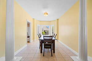 Dining space with light tile patterned flooring, decorative columns, and a textured ceiling