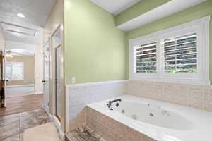 Bathroom featuring a stall shower, a tub with jets, tile walls, and a wainscoted wall