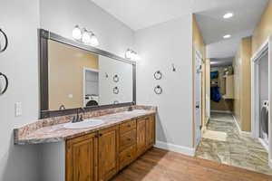 Bathroom with double vanity, a spacious closet, light wood-style flooring, and recessed lighting