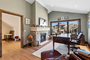 Office featuring lofted ceiling, wood finished floors, and a stone fireplace