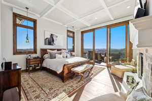 Bedroom featuring coffered ceiling, wood-type flooring, access to outside, a mountain view, and a high end fireplace